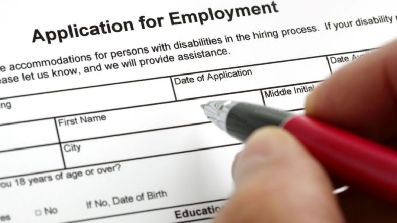 A hand with a pen filling out an application for employment